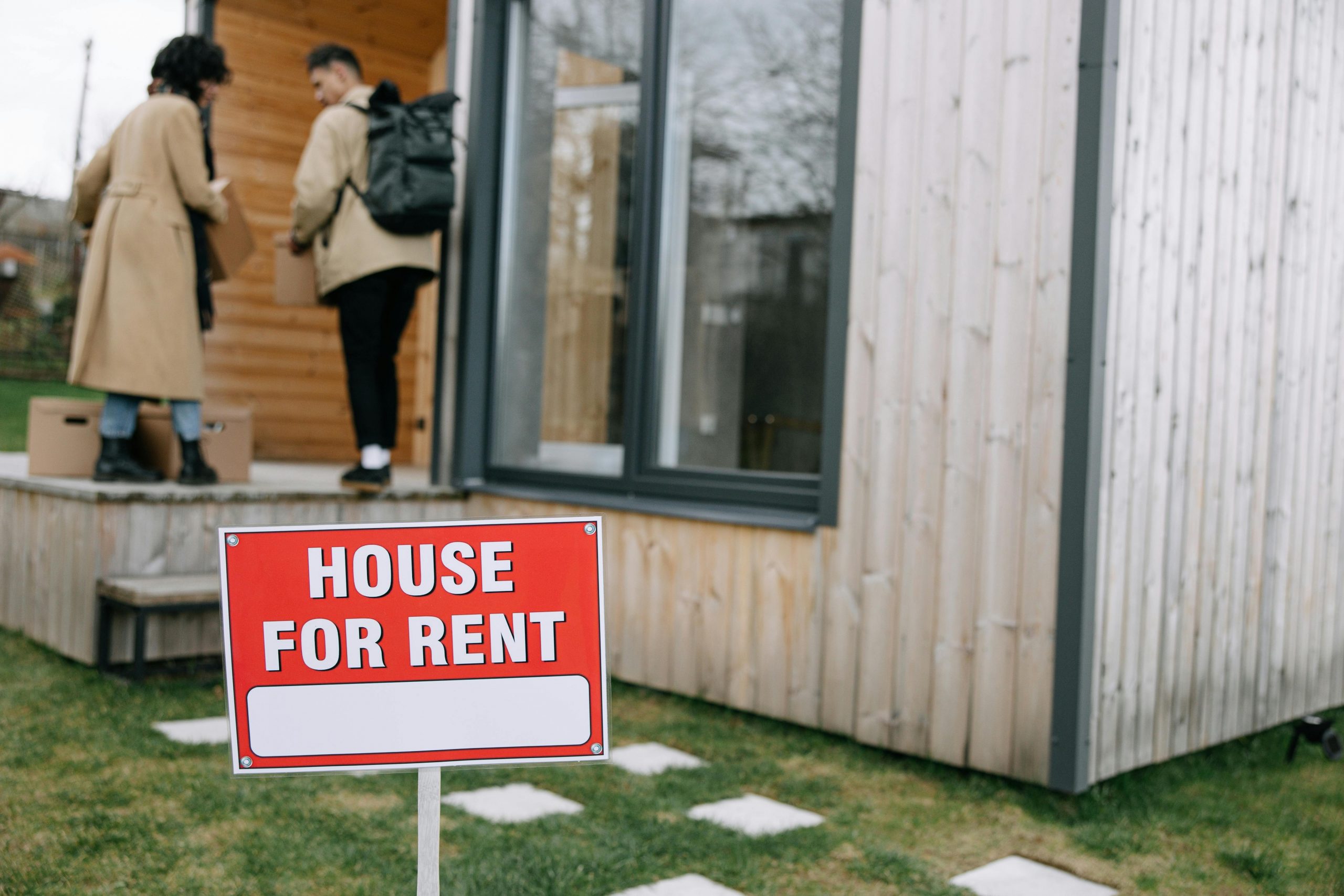 couple entering a home with a "house for rent" sign in the front yard