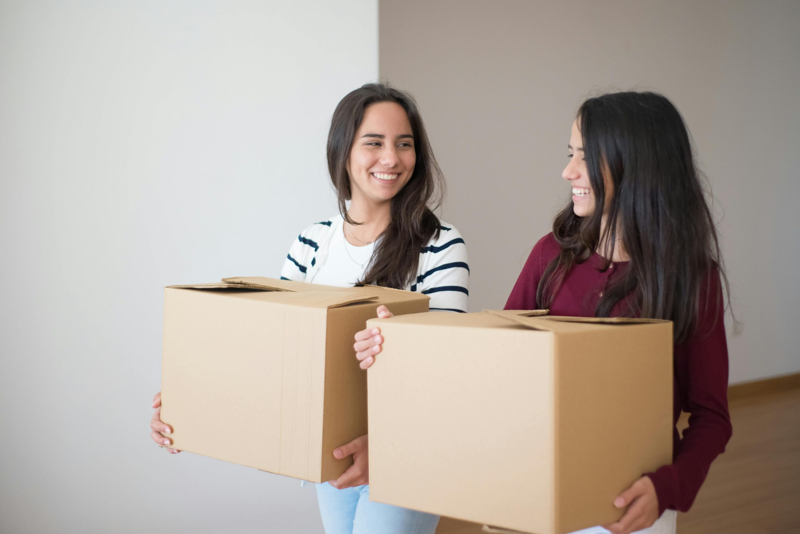 two women smiling at each other while carrying moving boxes